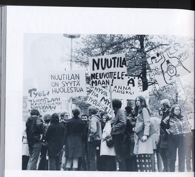 As a student Anna Mauranen was an active demonstrator. In June 1970 she took part in a demonstration in the Railway Square, in front of Mikonlinna, then the headquarters of Nokia. The figure of Matti Nuutila on the placard was the head of the Nokia cable factory and the deputy managing director of Nokia. A seven-week strike of metal workers was ongoing. In the picture Anna Mauranen is behind her cousin Marja Rosti in checked slacks. Source: Martti Häikiö's "Fuusio: Yhdistymisten kautta suomalaiseksi monialayritykseksi 1865–1982. Nokia Oyj:n historia 1", Edita 2001, p. 186.​