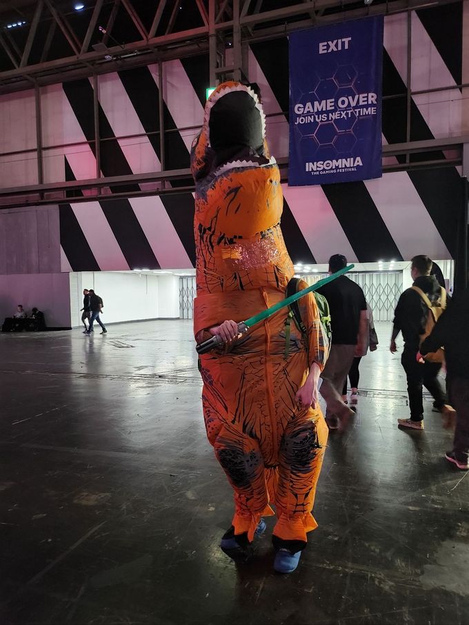 Someone wearing an inflatable T-Rex costume, holding a light sabre