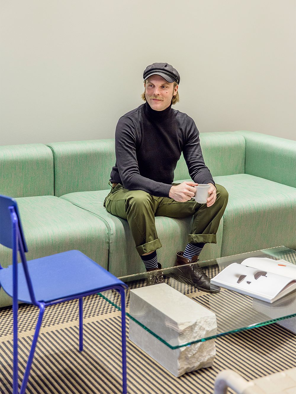 Design Sales Representative Matias Rahkola sitting on a green sofa with a cup of coffee in his hand at Finnish Design Shop's head office in Turku.