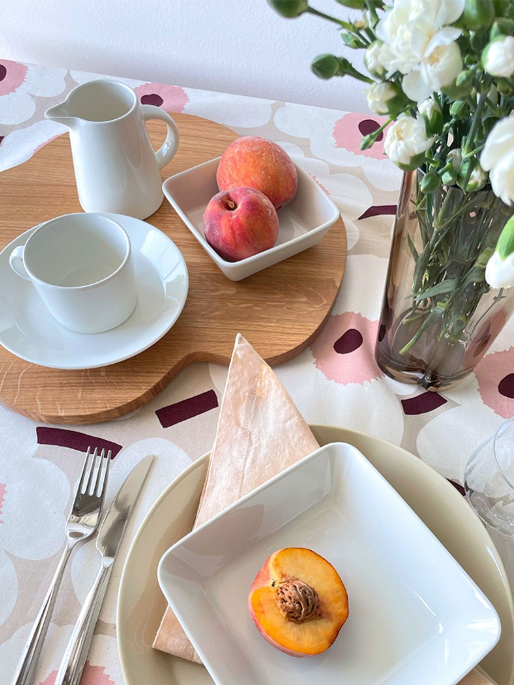 An image featuring Teema tableware, Carelia cutlery and Marimekko's Pieni Unikko fabric as a tablecloth in a table setting, as part of the dining area decor.