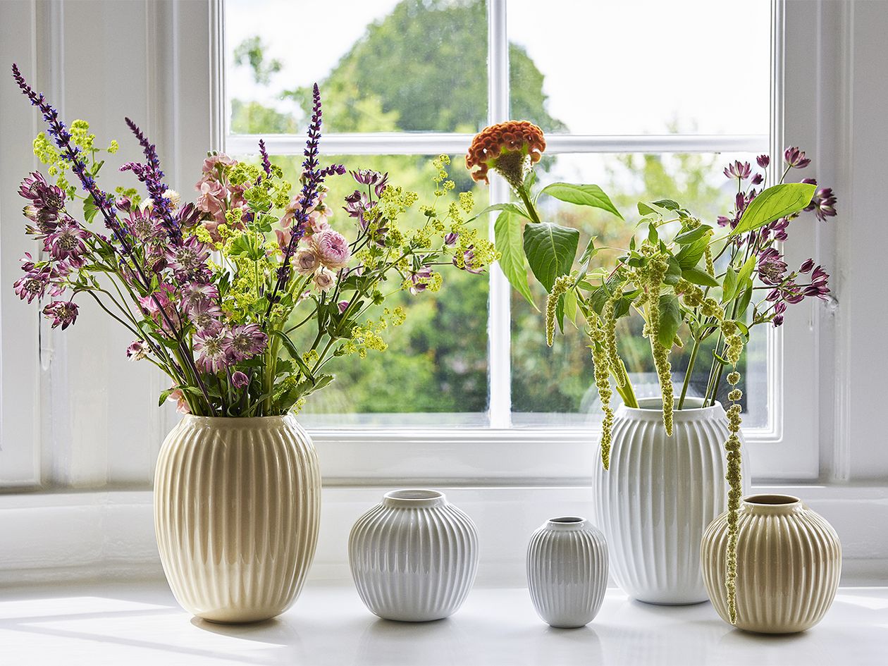 Different-sized and coloured Hammershøi vases in a row in front of a window