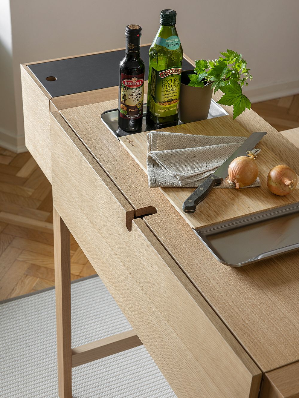 On top of Tapio Anttila's Jat-ko workstation are a onions cutting board and a knife as well as oil bottles and a herb pot.