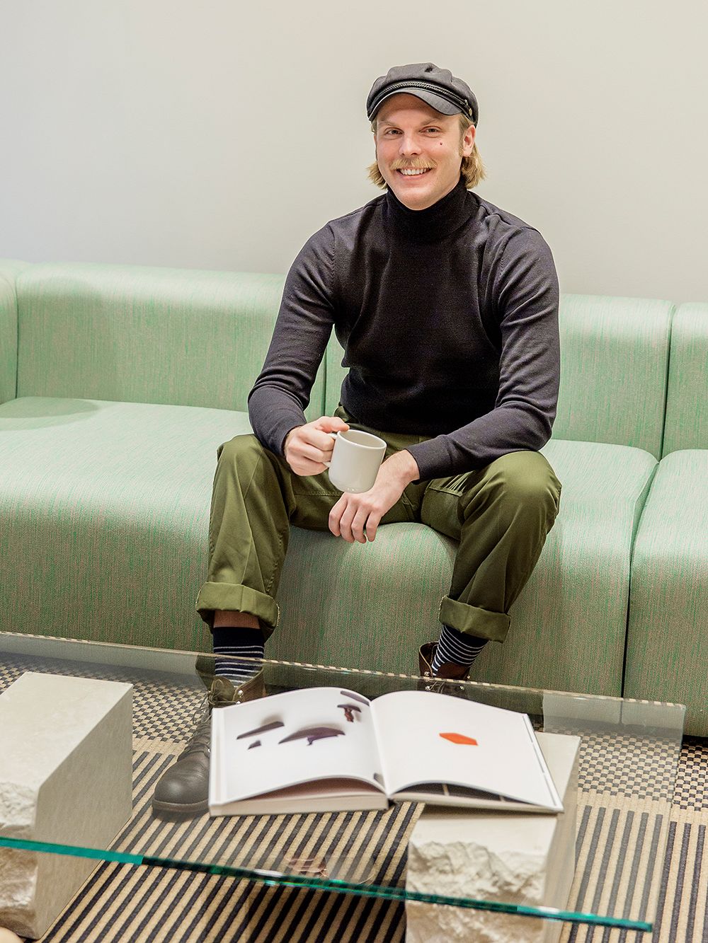 Design Sales Representative Matias Rahkola sitting on a green sofa with a cup of coffee in his hand.