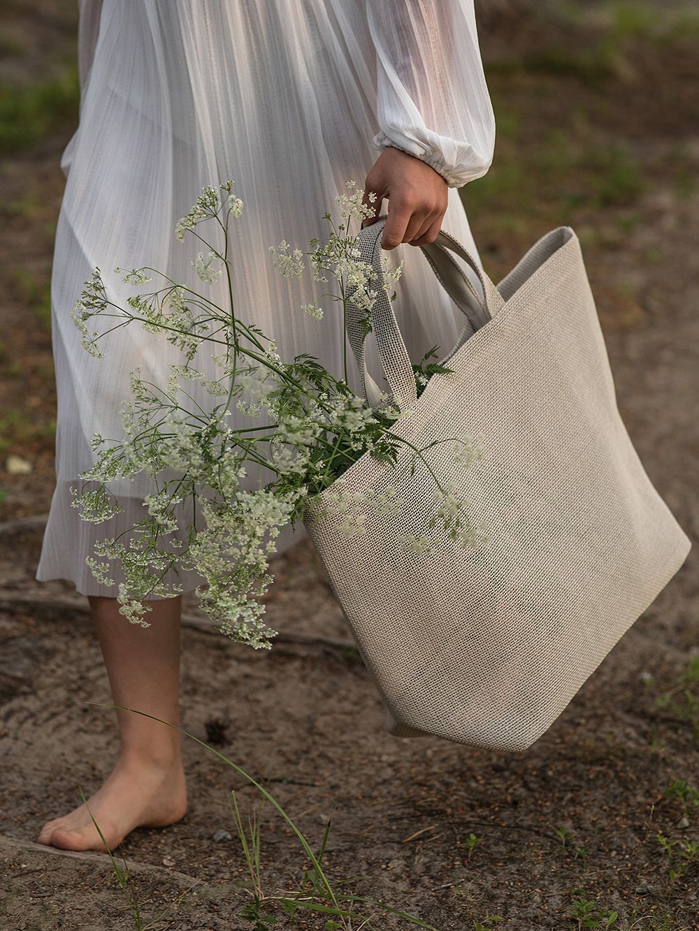 Woman carrying Woodnotes' beige Beach bag that has wild flowers in it