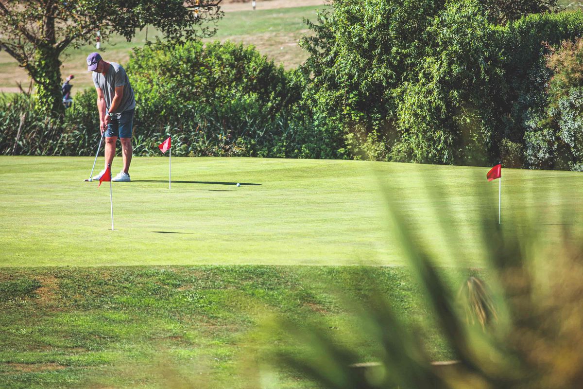 Golfeur en train de putter sur un green entouré de verdure, activité sportive et détente idéale pendant des vacances seniors Pierre & Vacances.