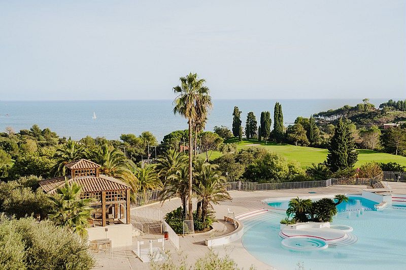 Vue sur le village de vacances Cap Esterel avec piscine, palmiers, terrain de golf et mer Méditerranée en arrière-plan