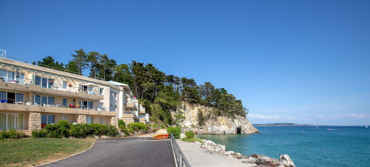 Résidence Cap Morgat en bord de mer, au pied d’une falaise boisée, avec promenade et vue sur l’eau turquoise