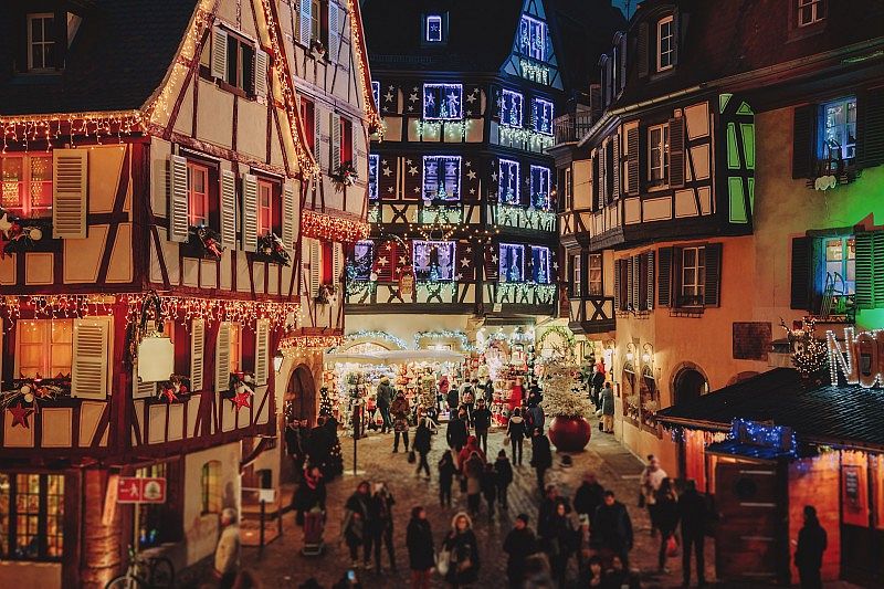Maisons à colombages illuminées et foule déambulant dans le marché de Noël de Kaysersberg de nuit.
