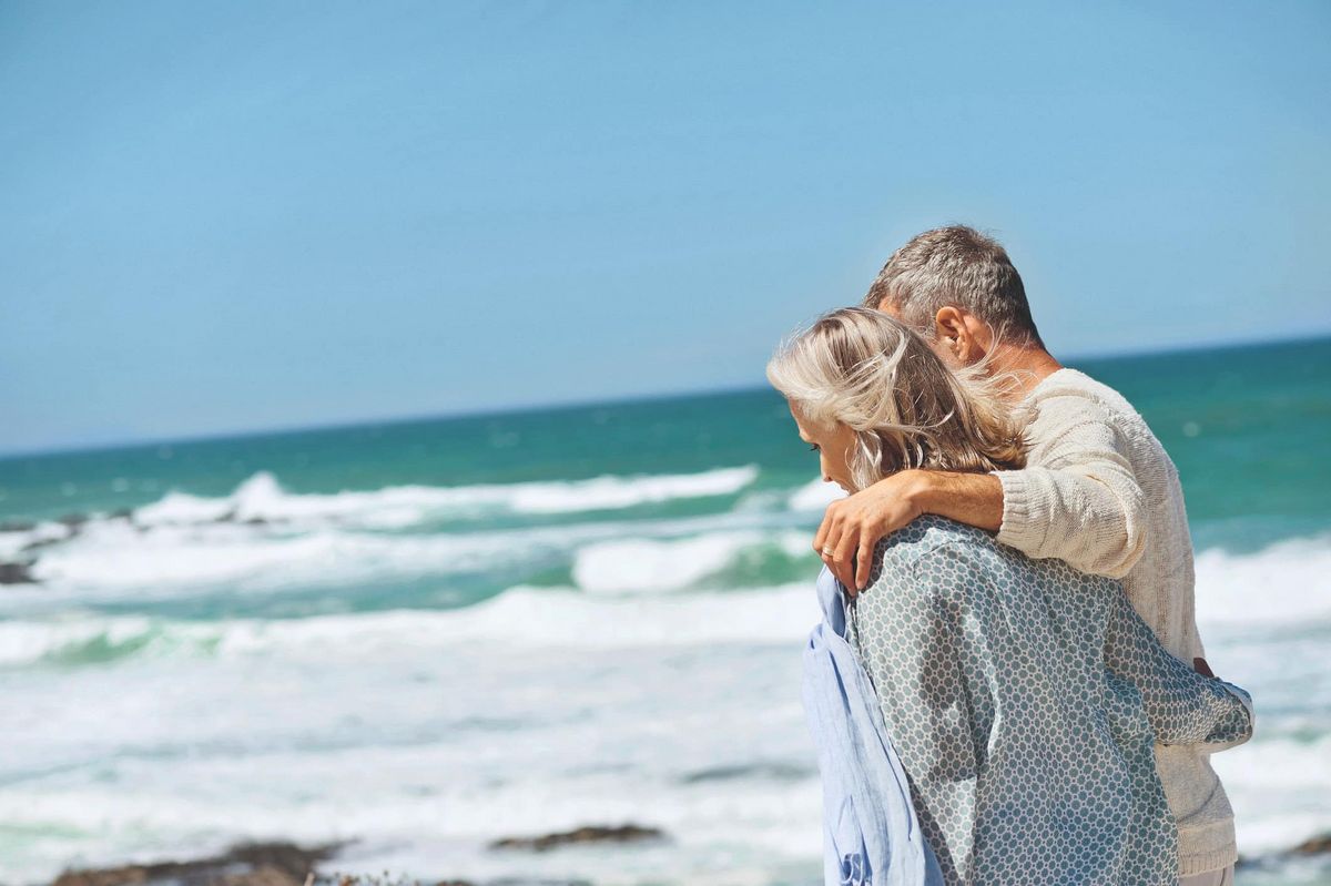 Un couple de seniors se tiennent par les épaules en contemplant la mer
