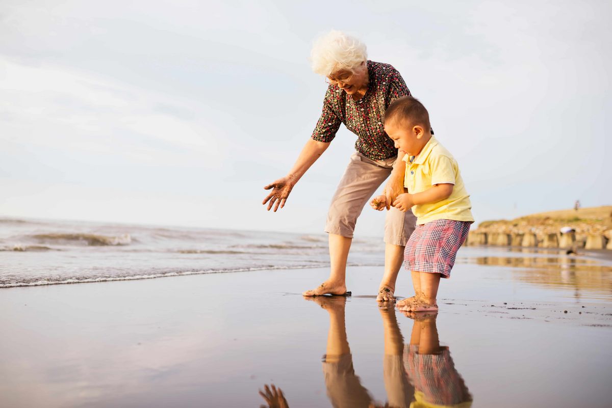 Une grand-mère joue avec son petit fils sur une plage les pieds dans l'eau