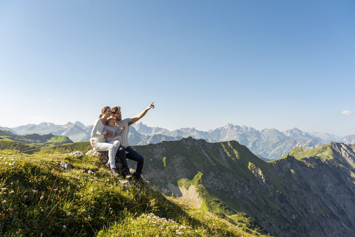 Couple de parent avec leur bébé assis sur le haut d'une montagne contemplant la vue