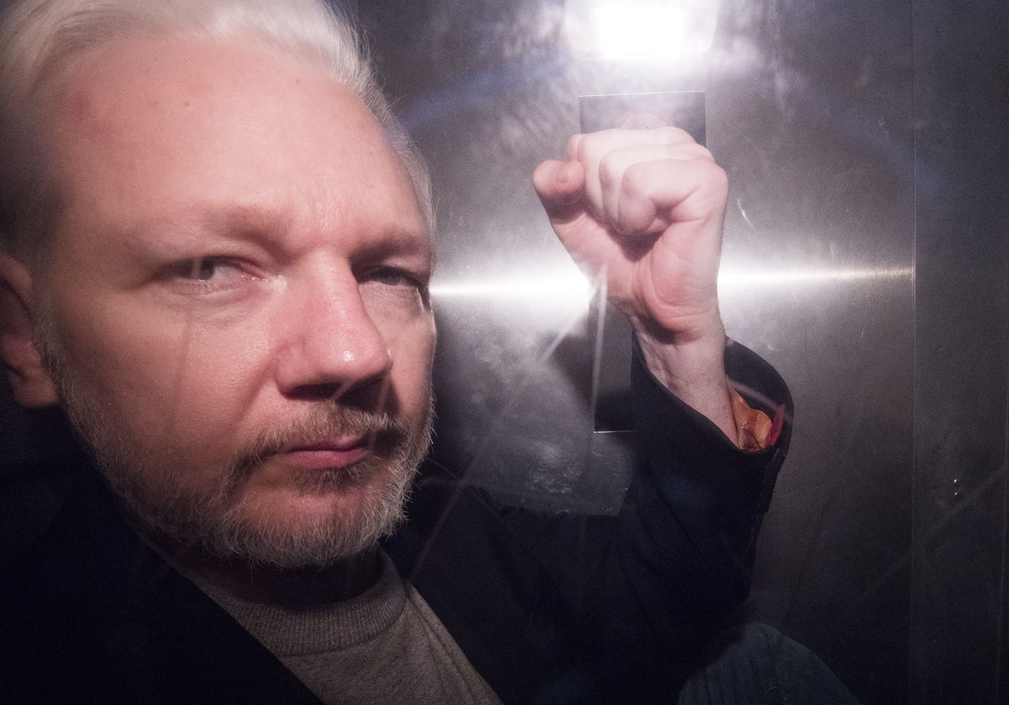 Julian Assange elehti poliisiauton lasin takaa valokuvaajille saatuaan 50 viikon vankeustuomion huhtikuussa Lontoossa.