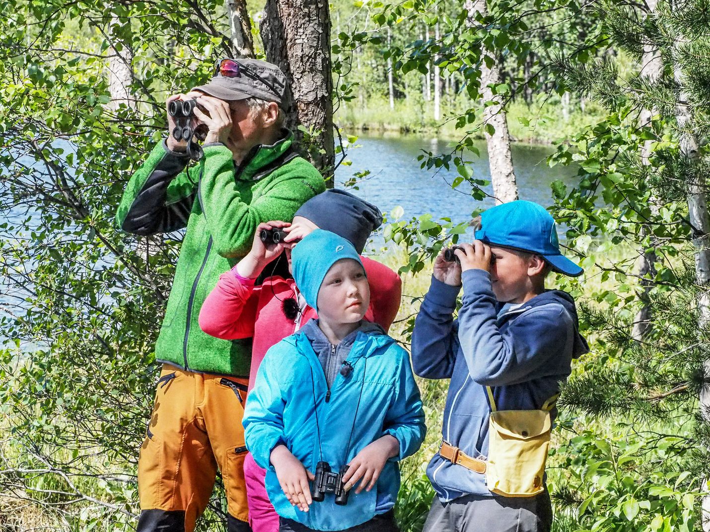 Pirkka-Pekka Petelius, Oskari Järvelä, Mea Packalén ja Nuppu Tammi kiikaroivat lintuja. He näkevät järvellä muun muassa naurulokkeja.