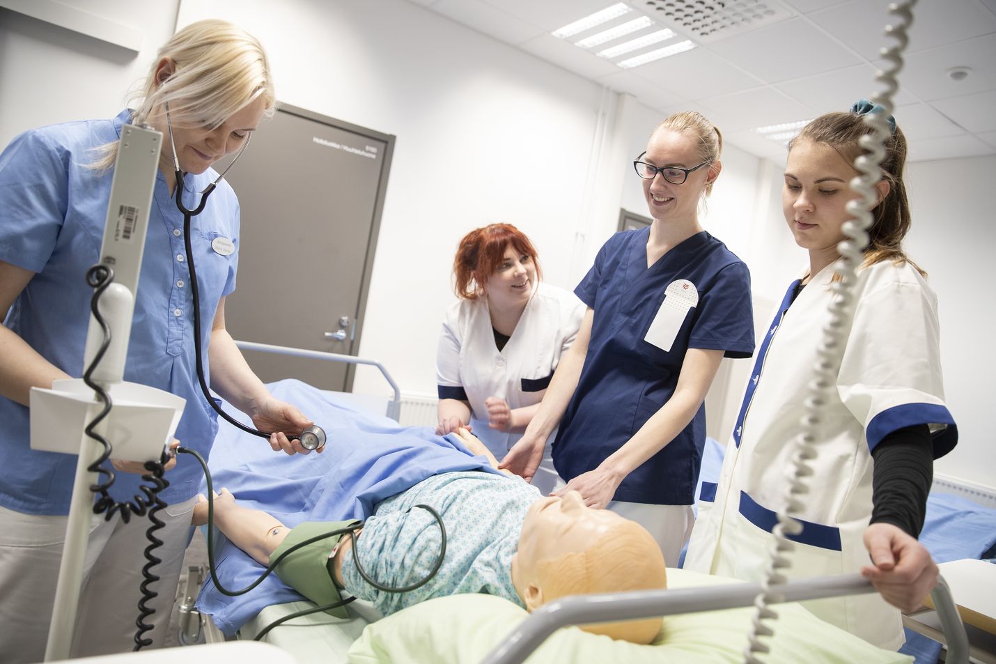 Lähihoitajaksi opiskelevat Johanna Stenroos (vasemmalla), Kamilla Lehtonen, Henna-Sofia Pohjola ja Nella Agge harjoittelevat hoitotoimia nuken kanssa.