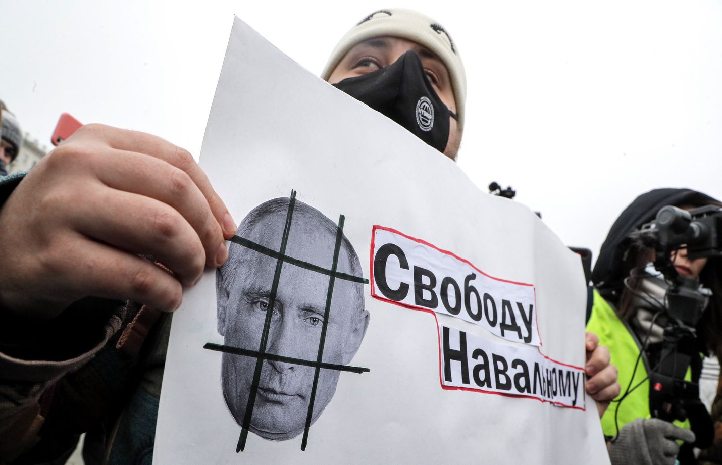 Protestoija pitelee lappua, jossa vaaditaan vapautta Navalnyille. Kaltereiden taakse toivotetaan puolestaan Putinia.
