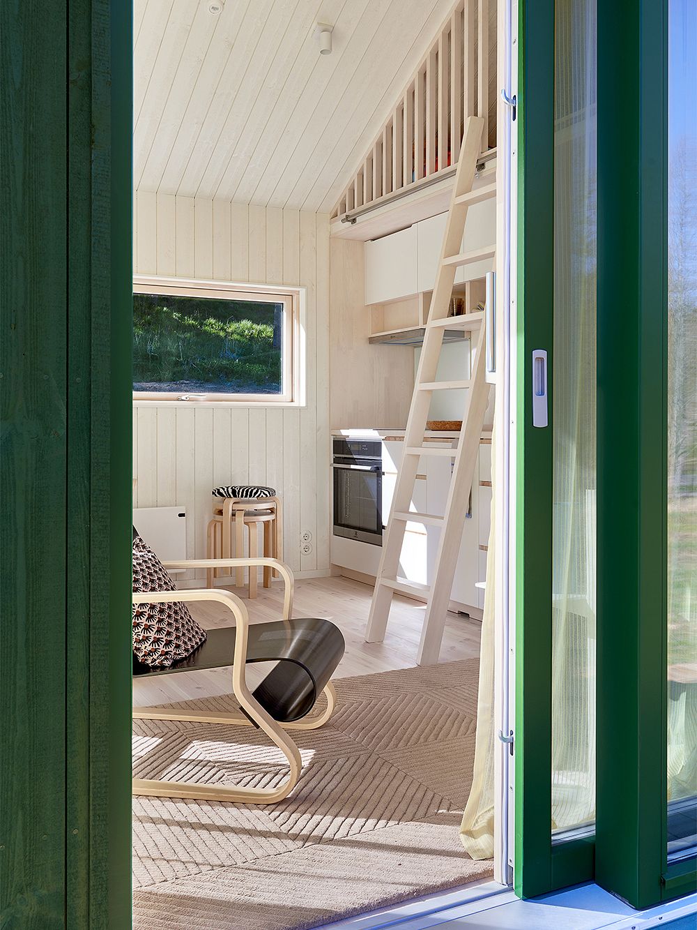 Kuva, jossa Fiskars Biennalen Arkkitehdin talo -näyttelyssä mukana oleva Sommarnöjenin Sommar 30 -mökki: olohuoneen sisustus ja keittiö.
