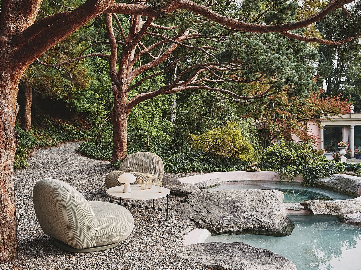 An image of GUBI's Pacha Outdoor armchairs and TS Outdoor coffee table in the garden.