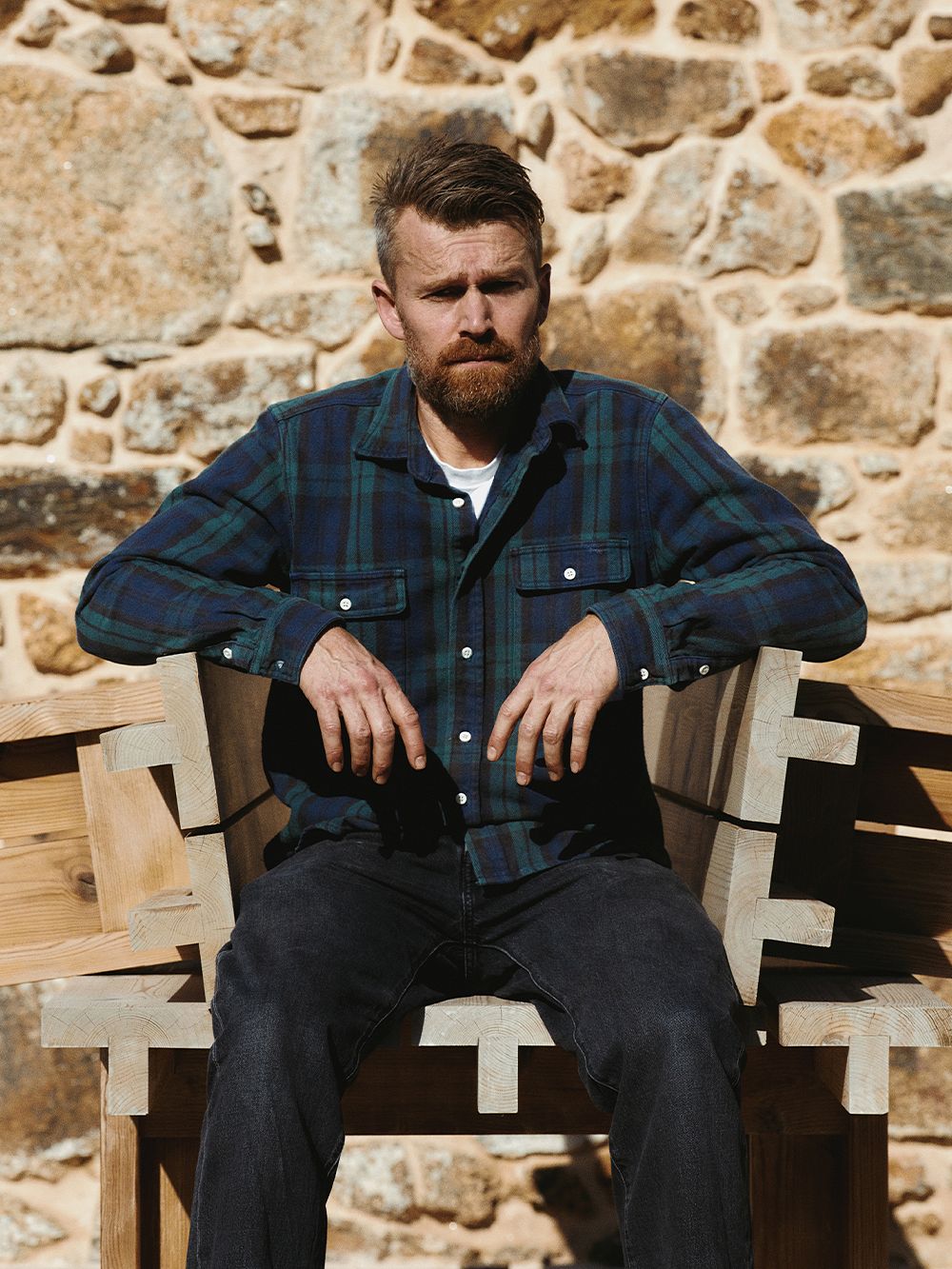 Muotoilija Henrik Tjærby istuu Vaarniille suunnittelemansa Osa-puutarhapöydän päällä