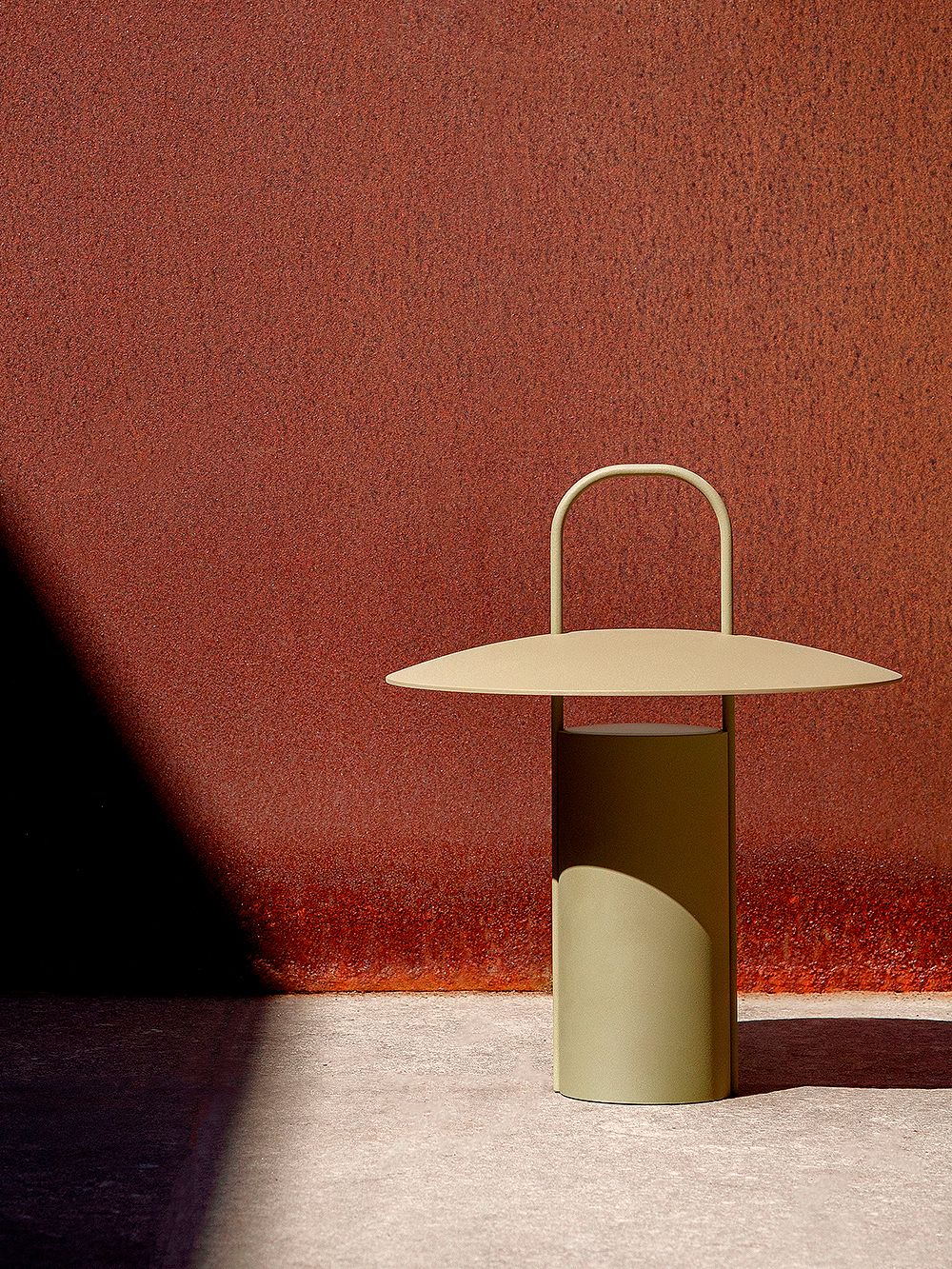 An image of Menu's dusty green Ray table lamp against a red background.