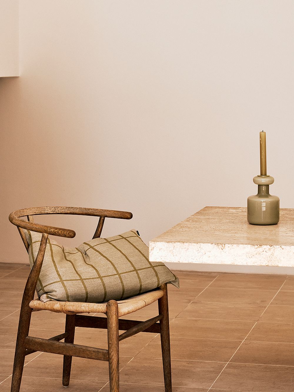 Kuva, jossa Marimekon Tiiliskivi-tyynynpäällinen Carl Hansen & Sønin Wishbone-tuolin päällä osana sisustusta. Kuvassa myös kivinen pöytätaso, jonka päällä Marimekon Plunta-kynttilänjalka.