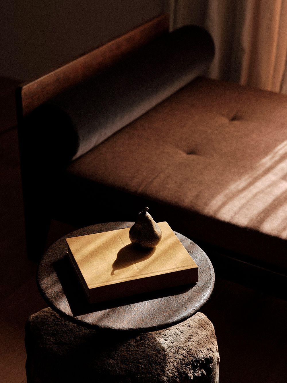 Kuva, jossa MENUn päärynää muistuttava Sentiment-paperipaino kirjan päällä sohvapöydällä, osana olohuoneen sisustusta.