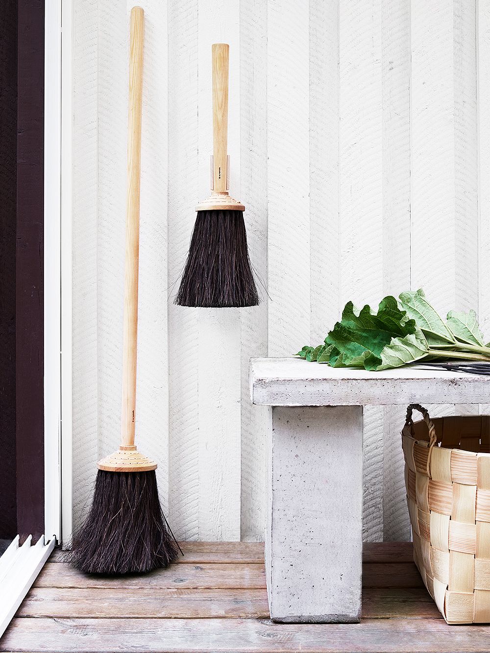 An image of Iris Hantverk's long porch broom and short porch broom leaning against the summer cottage wall, as part of the summer house decor.