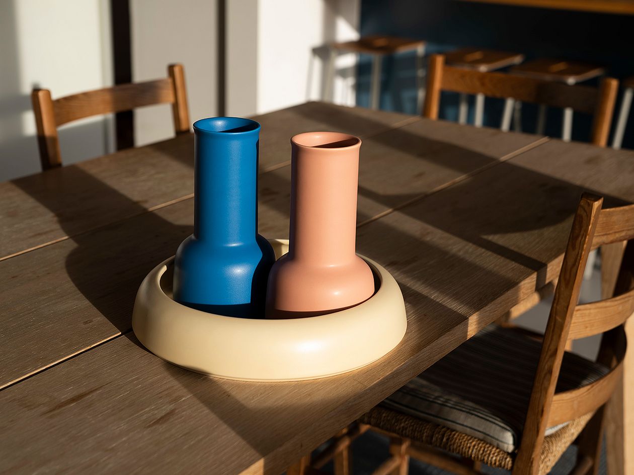 An image of Raawii's Omar nude carafe and electric blue carafe placed on the table with a soft yellow bowl, as part of the summer home decor.