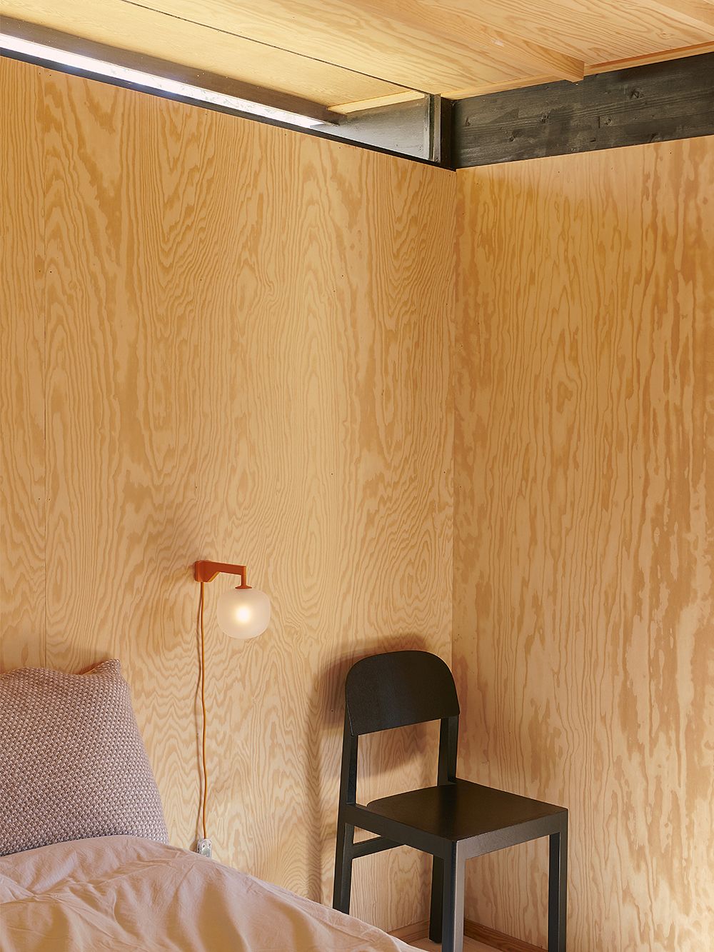 Kuva, jossa kesämökin makuuhuone ja Muuton oranssi Rime-seinävalaisin ja musta Workshop-tuoli.