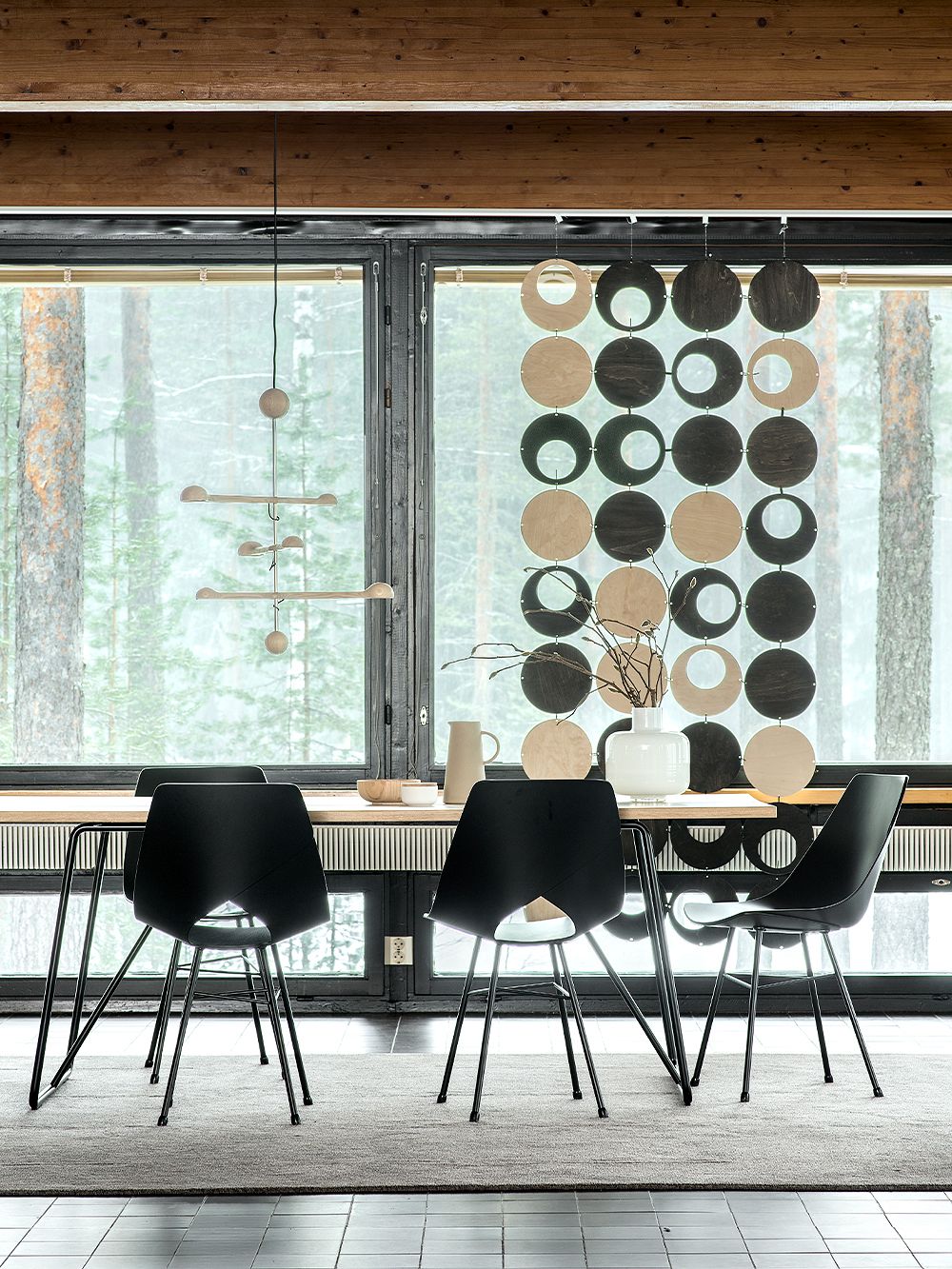 Ruokailutilassa Tapio Anttila Collectionin Front Country Oak -ruokapöytä ja sen ääressä mustat Limi-tuolit. Taustalla ikkuna, josta avautuu metsämaisema, ja ikkunan edessä verhona Palapala-tilanjakaja.