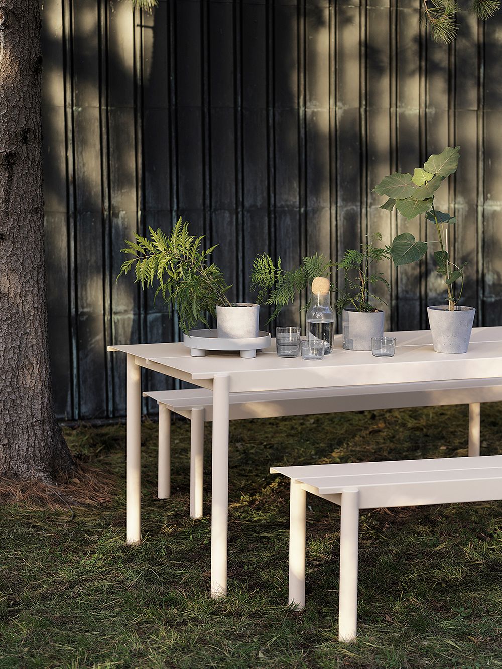 Kuva, jossa Muuton Linear Steel -ruokapöytä ja penkit kesämökin puutarhassa, osana kesämökin sisustusta.