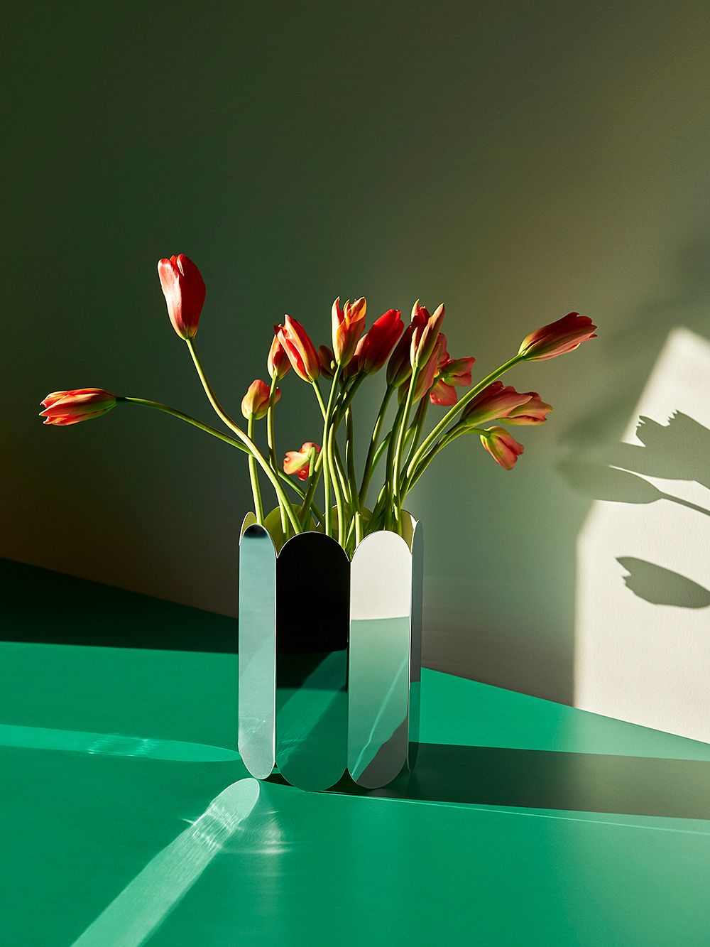 HAYn peilipintainen Arcs-maljakko täynnä tulppaaneita, vihreällä pöydällä.