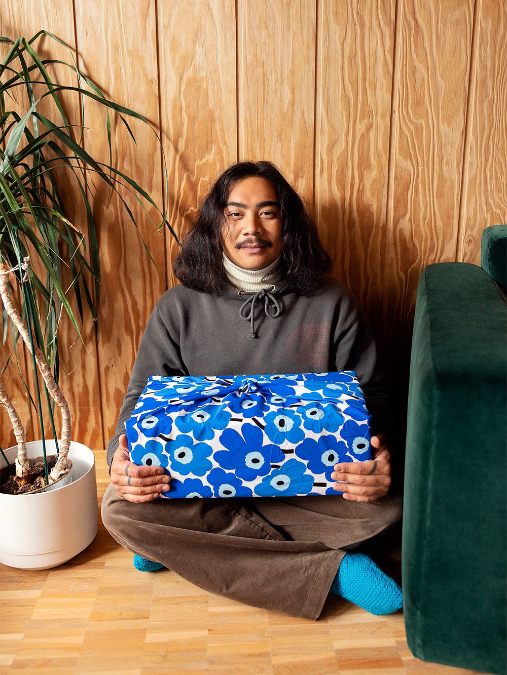 A person holding a large gift wrapped in Marimekko's Unikko fabric.