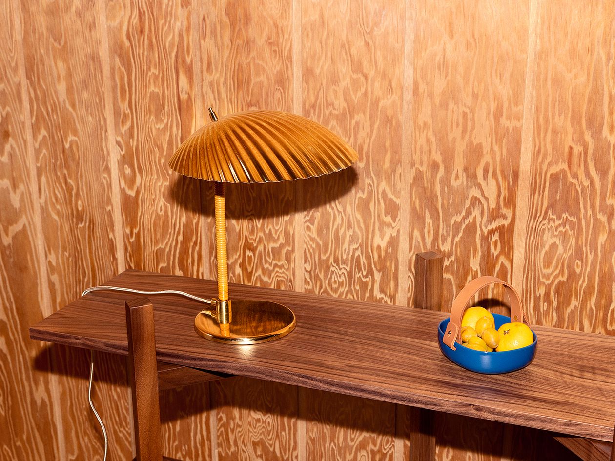 An image featuring Paavo Tynell's 5321 table lamp also known as the Shell and Marimekko's Pieni Koppa serving dish in blue, as part of the living room decor.