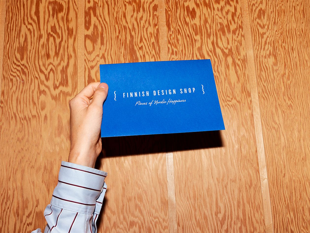 Kuva, jossa käsi pitelee sinistä kirjekuorta, jossa lukee valkoisella kirjoituksella "Finnish Design Shop".