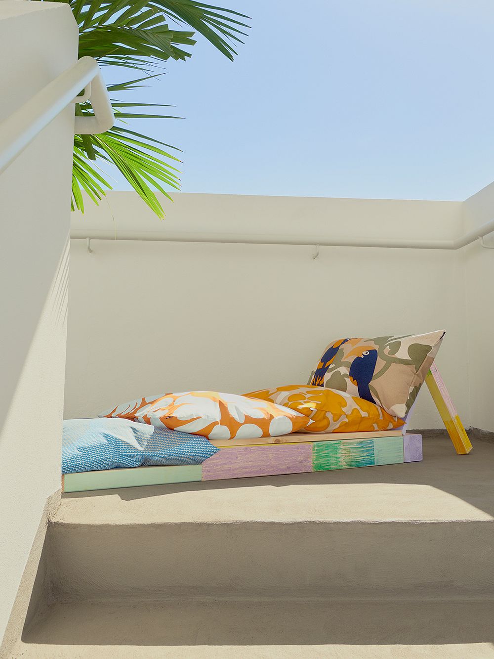 An image of a daybed on a sun-drenched terrace, filled with Marimekko's cushion covers placed.