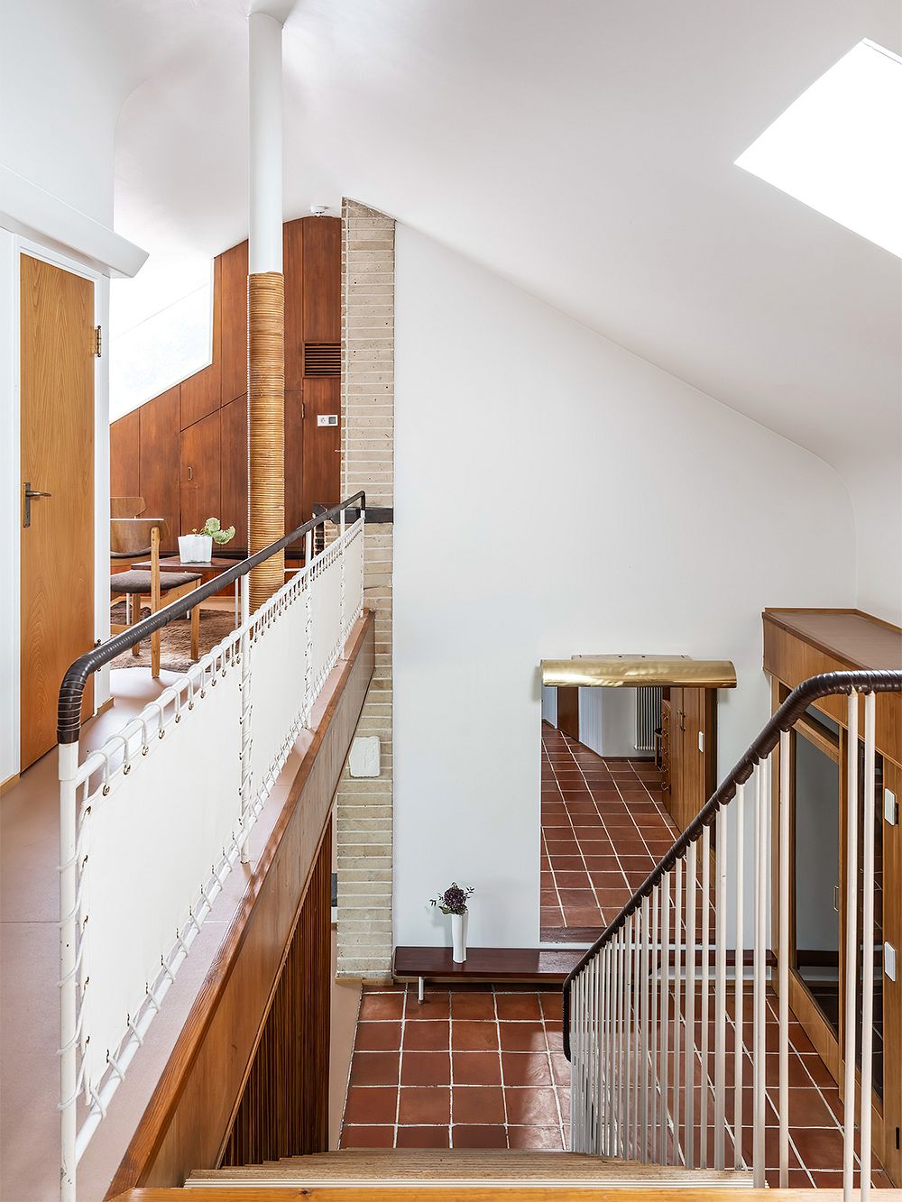 An image featuring Villa Ervi designed by architect Aarne Ervi. The photo shows the interior of the downstairs lobby with a staircase leading downwards.