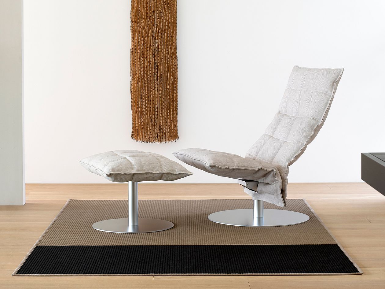 Woodnotes' K chair and K ottoman in a shade of stone, placed in a living room.