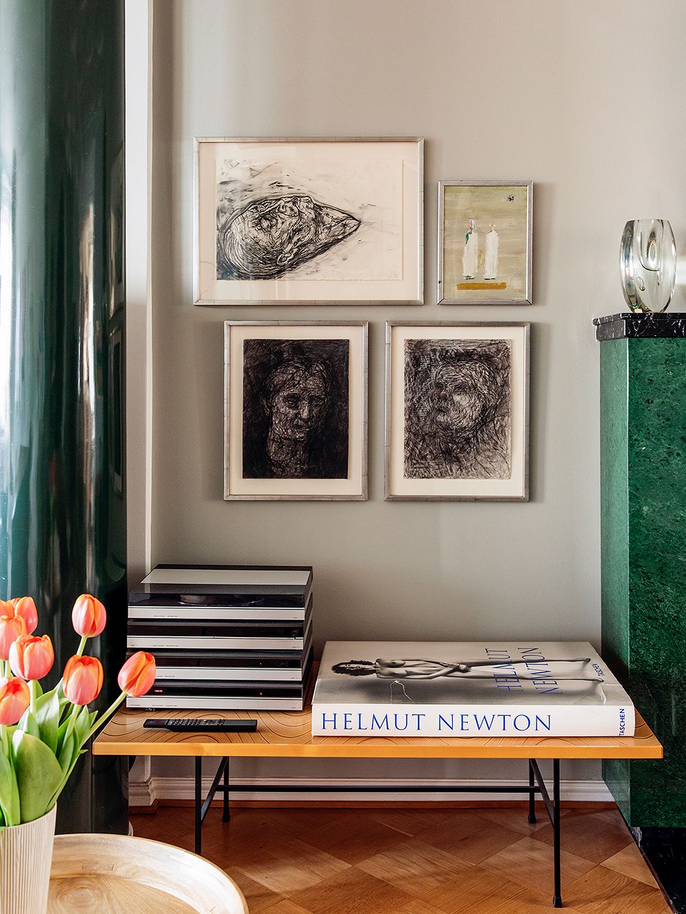 An image of painting and drawings on the wall. Also a small table, that has books placed on it.
