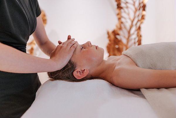 Une femme allongée sur une table de massage reçoit un soin relaxant au visage dans un spa.