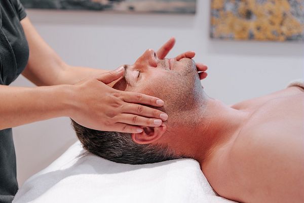 Un homme reçoit un massage relaxant au spa, allongé sur une table de soin, les yeux fermés, profitant d'un moment de détente et de bien-être.