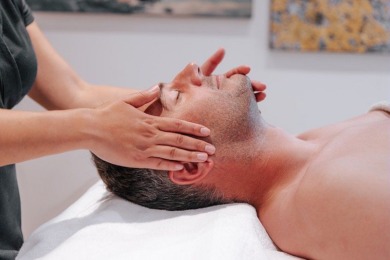 Un homme reçoit un massage relaxant au spa, allongé sur une table de soin, les yeux fermés, profitant d'un moment de détente et de bien-être.