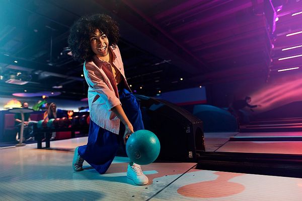 Une femme jouant au bowling, concentrée et souriante, dans une ambiance lumineuse et colorée.