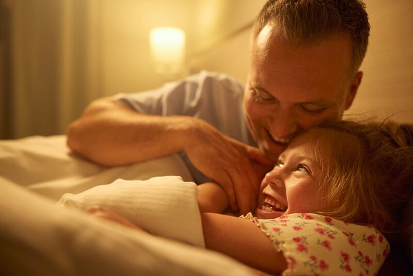 Un père câline sa fille dans son lit, partageant un moment de complicité et de rires