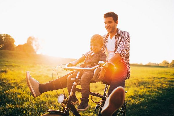 Un père et son enfant profitent d'une balade à vélo au coucher du soleil, partageant un moment complice et joyeux en pleine nature.