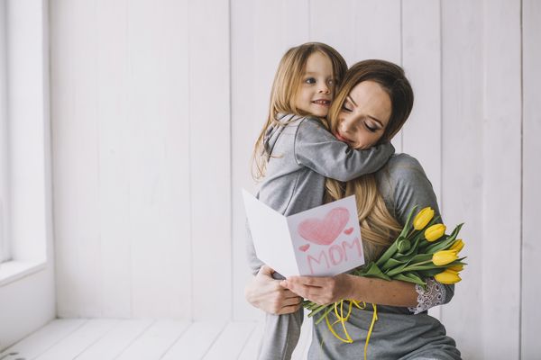 Une mère embrassant sa fille avec un bouquet de tulipes et une carte de fête des mères.