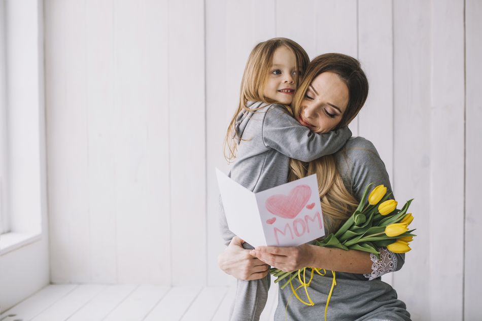 Une mère embrassant sa fille avec un bouquet de tulipes et une carte de fête des mères.