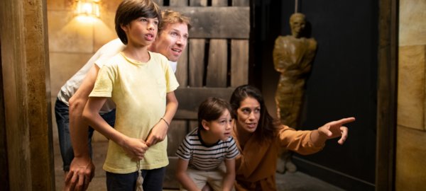Une famille participe à un escape game, concentrée et coopérative pour résoudre les énigmes. L'ambiance est immersive avec un décor mystérieux et des éléments intrigants.