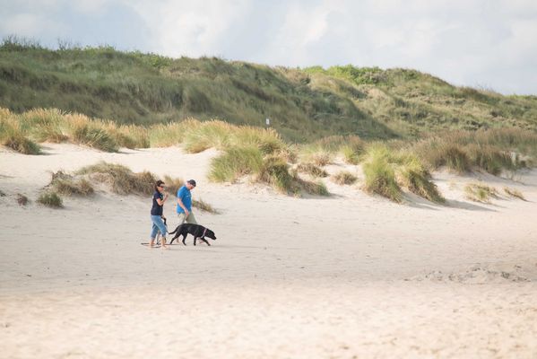 Couple marchant avec leur chien sur une plage de sable en Normandie, escapade romantique en pleine nature