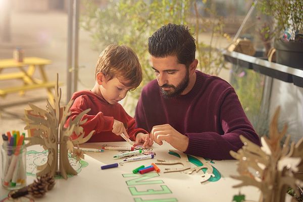 Un père et son fils font du coloriage sur une table avec des feutres.