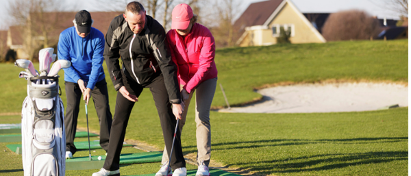 Au premier plan un homme âgé et une femme âgée s'entraîne au golf.